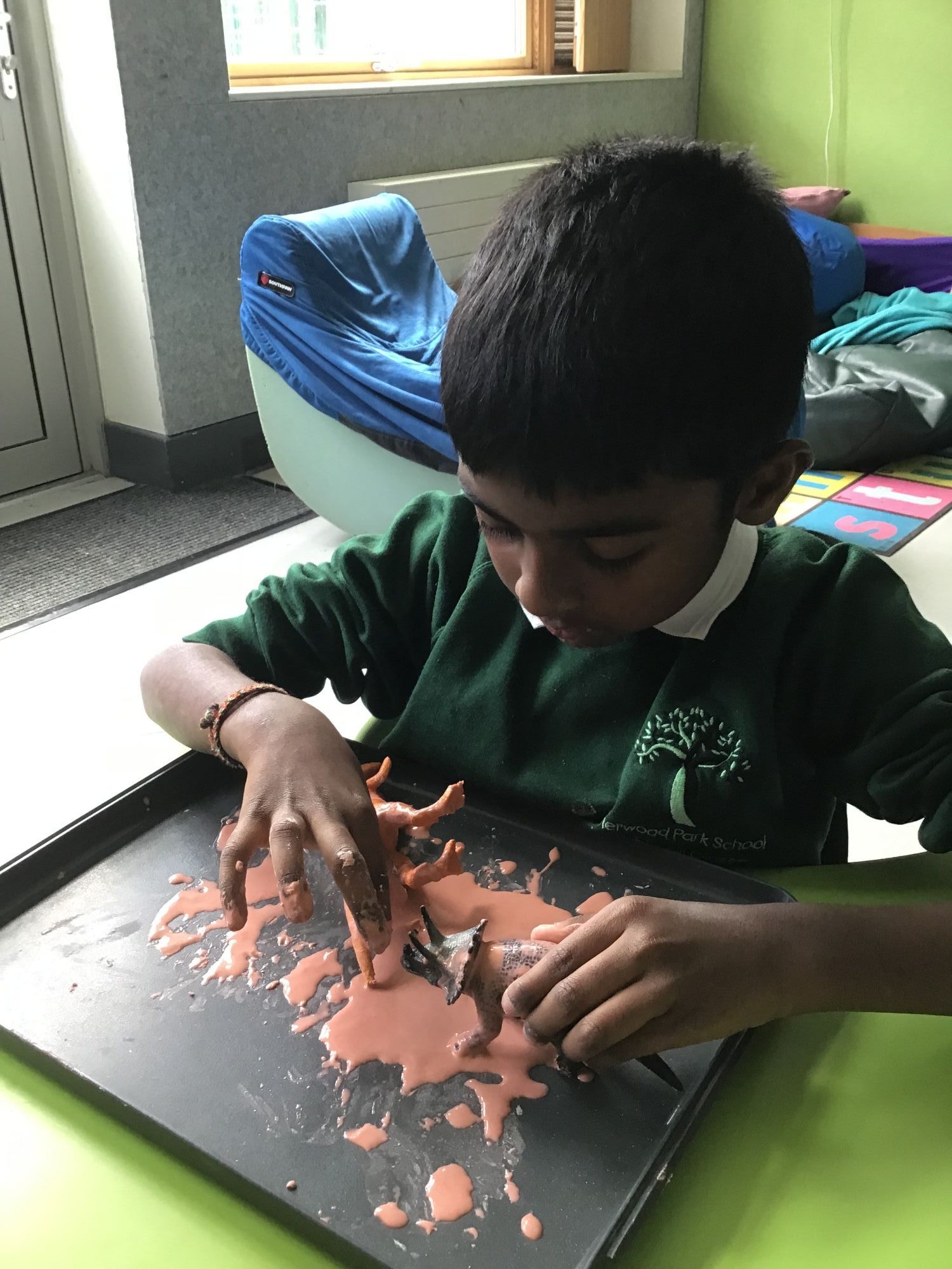 Pupil doing an activity with paint and a toy dinosaur 